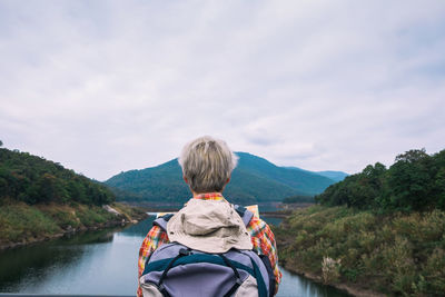 Rear view of man looking at river against mountains