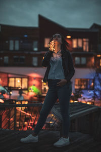 Full length of young woman holding illuminated lights while standing against building at night