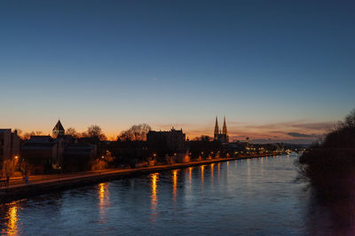 River by illuminated buildings against sky at dusk