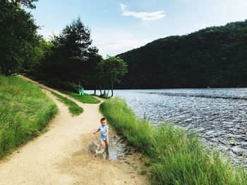 Boy running by grass and lake against sky