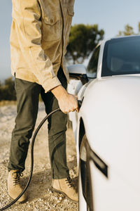 Man charging electric car during road trip