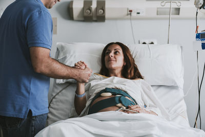 Man consoling pregnant woman on bed at hospital