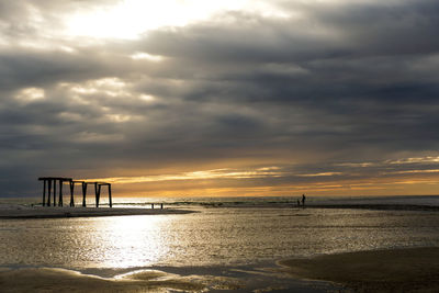 Father and child watching abandoned structure during sunset on the coastline 