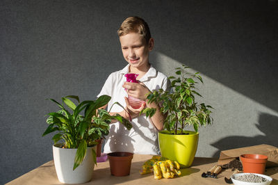 Cute boy takes care of indoor flowers, spray plants, maintain the necessary humidity level