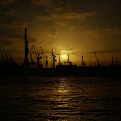 Silhouette cranes at commercial dock against sky during sunset