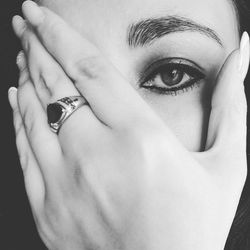 Close-up portrait of young woman covering face with hand against black background