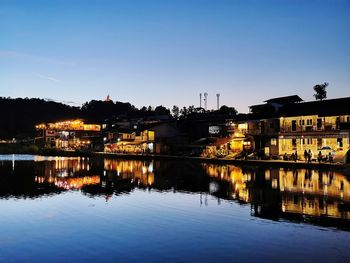 River by illuminated buildings against sky at dusk
