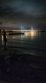 Illuminated bridge over sea against sky at night