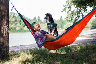 Man swinging with dog on hammock against trees in forest