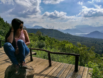 Man sitting on railing against mountains and sky