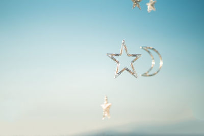 Stars and half moon float on a pastel blue and white background.