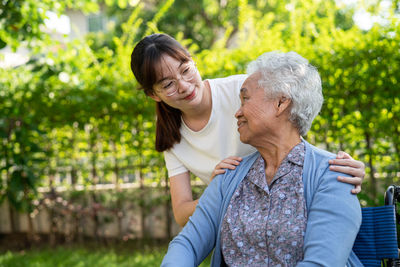 Caregiver help and care asian senior or woman patient sitting and happy on wheelchair in park,  