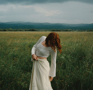 Young woman standing on field against sky