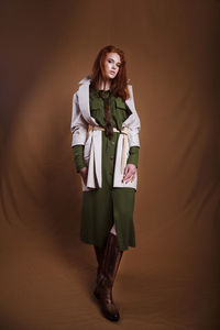 Portrait of young woman standing against brown background