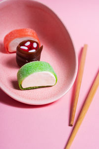 Appetizing colorful sweet sushi served on ceramic plate with wooden chopsticks placed on pink background