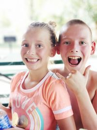 Portrait of cheerful siblings sitting against window at home