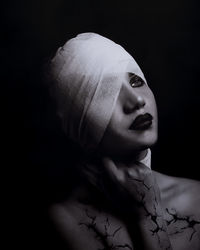 Close-up of topless thoughtful young woman face wrapped in bandage against black background