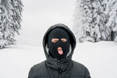 Man with ski mask sticking out tongue in winter forest