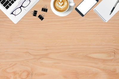 Directly above shot of coffee cup by laptop and mobile phone with book on table