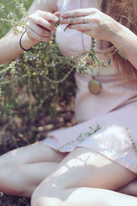 Midsection of woman holding plant while relaxing on field