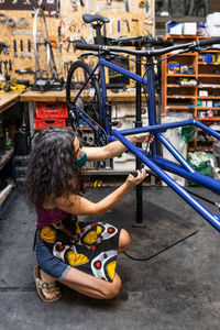 Side view of female worker in protective mask installing break and transmission wires on bicycle during maintenance service in workshop