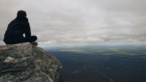 Woman sitting at the edge of mountain against cloudy sky