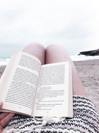 Low section of woman on book at beach against sky
