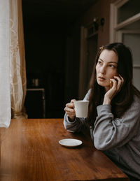 Freelance woman with the coffee and mobile phone at home talking expressive