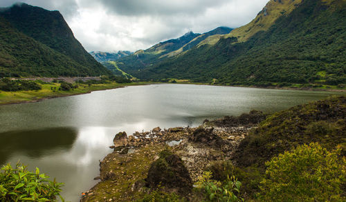 Scenic view of lake by tree mountains against cloudy sky