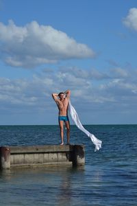Shirtless man with scarf standing on pier over sea