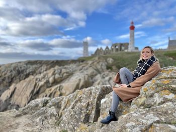 Portrait of teenage girl sitting on rock against sky