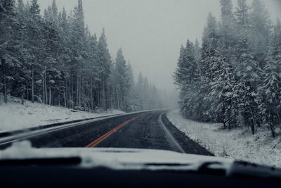 Road amidst trees seen through car windshield during winter