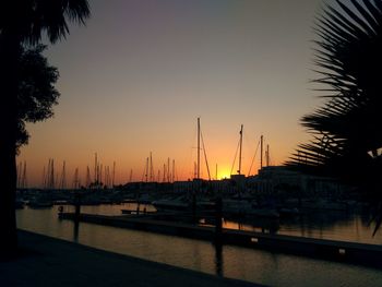 Sailboats moored at harbor against sky during sunset