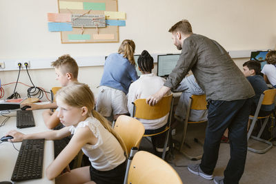 Male teacher with students learning through computers in classroom at school