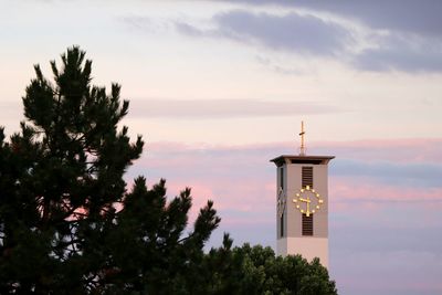 Low angle view of lighthouse by building against sky during sunset