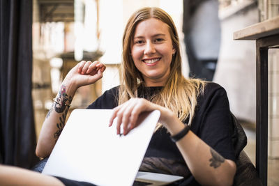 Portrait of happy young businesswoman with laptop sitting on bean bag in small office