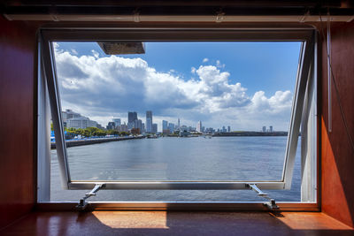 Buildings by sea against sky seen through glass window