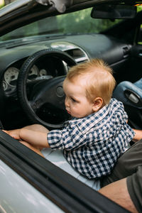 Dad shows his little son how to drive car while sitting behind wheel