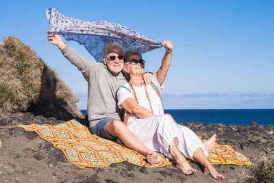 Couple in sunglasses with scarf sitting at beach