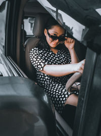 A girl wearing a polkadot dress, sun glasses and high boots sitting in a car 