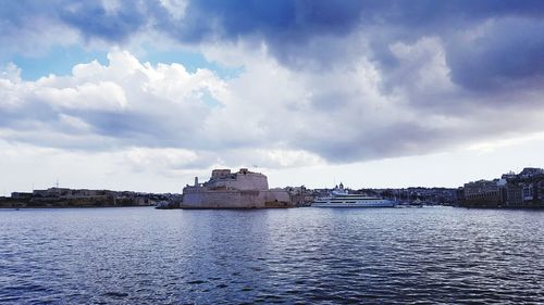 Buildings by sea against cloudy sky