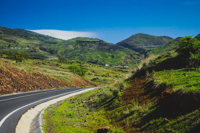 Road amidst green landscape against blue sky