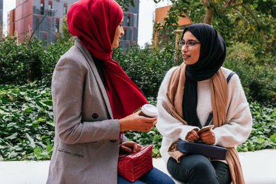 Friendly arab female friends sitting on street and talking to each other while enjoying weekend together