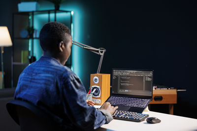 Rear view of man using laptop at home