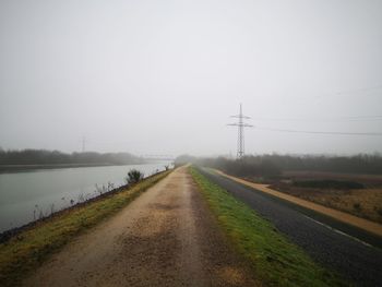 Road amidst field against sky during foggy weather