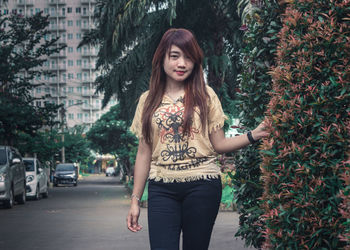 Portrait of smiling young woman standing by plants on street