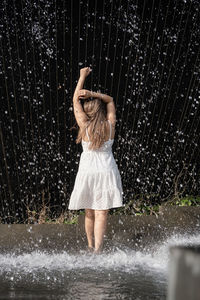 Side view of young woman standing against waterfall