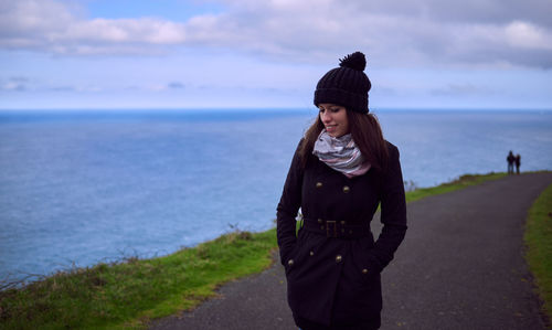 Young woman standing on sea shore against sky