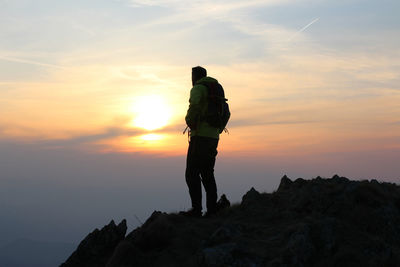 Man standing on rock against sky during sunset