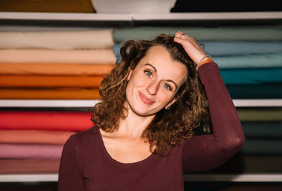 A content fashion designer with curly hair poses casually in her studio